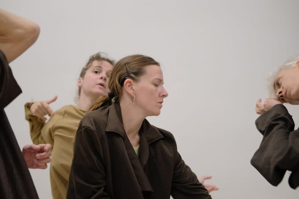 Four female dancers are positioned across a beige background. They negotiate the visible, revealing and obscuring their faces in a constant state of becoming