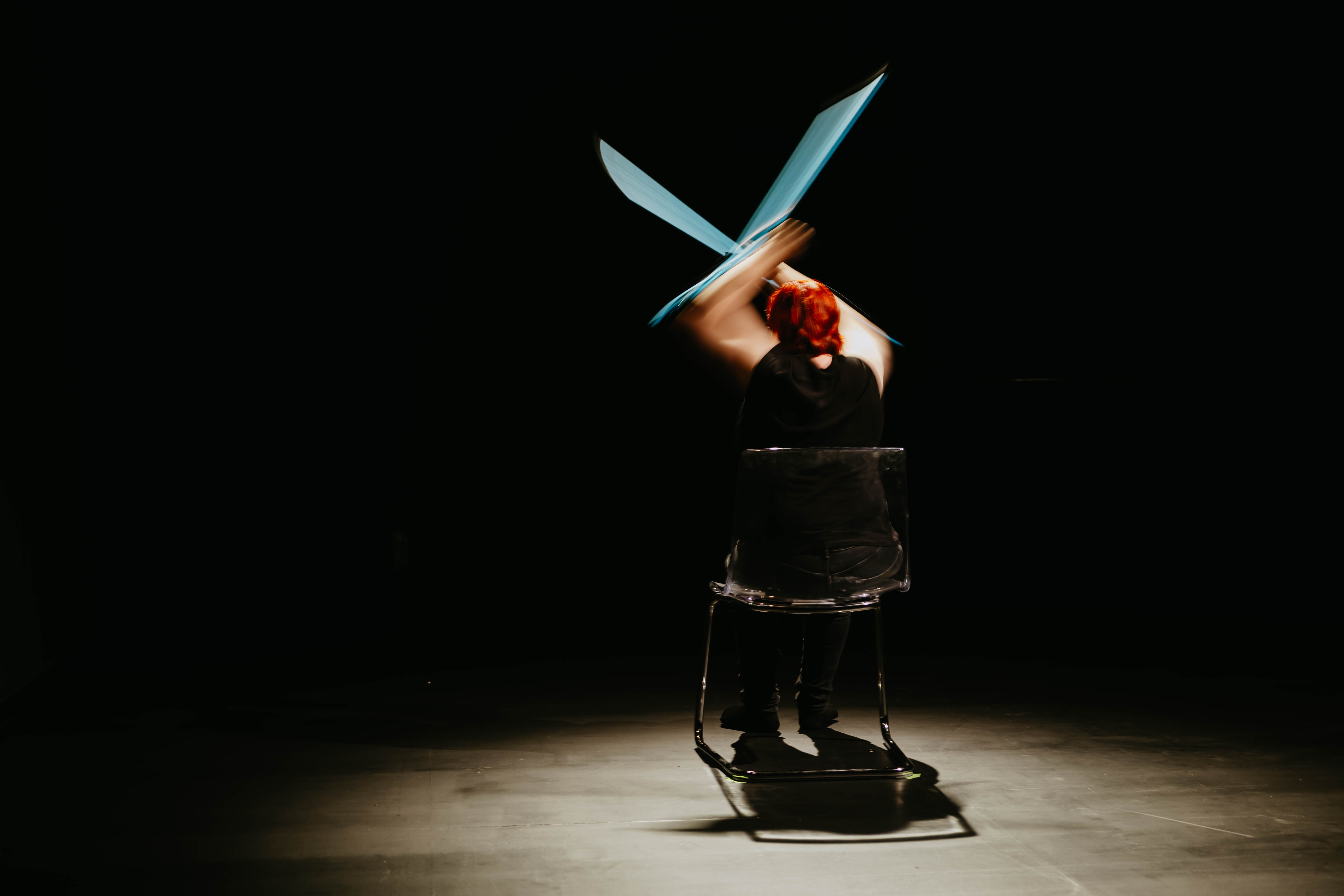 Demy sitting on a chair with her back to us lifts her blue crutches above her haid