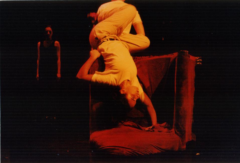two performers on a red chair, the one is upside down